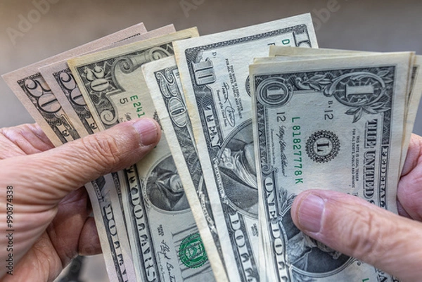 Fototapeta Close-up of a man counting US dollars banknotes on his hands, against plain background. One, ten, twenty and fifty dollar denominations.