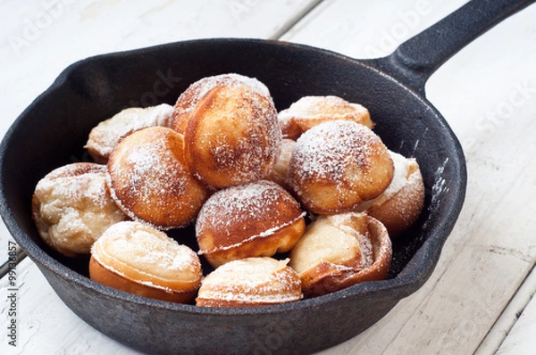 Obraz Danish style aebleskiver apple pancakes or pancake puffs served in a cast iron pan on white rustic boards.