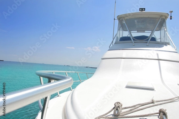 Obraz A close-up view of the front deck of a sleek white luxury yacht cruising over a crystal-clear turquoise sea under a bright blue sky. Perfect image for travel, tropical vacation, maritime lifestyle, or
