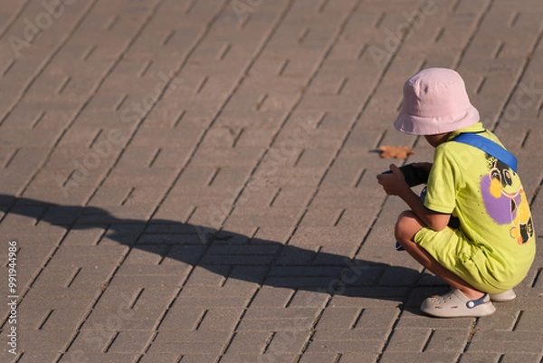 Fototapeta teenage boy in bright clothes on the street squatting and looking at smartphone