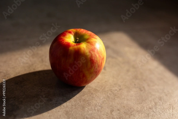 Fototapeta close-up of a red and yellow apple against a brown stone in moody lighting