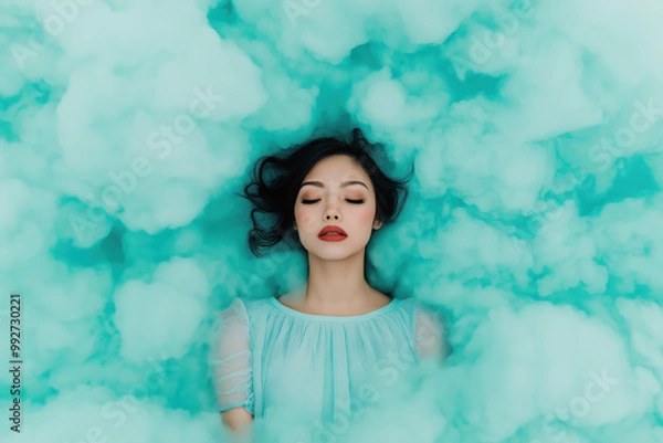 Fototapeta Dreamy portrait of a woman lying in soft blue clouds with peaceful expression