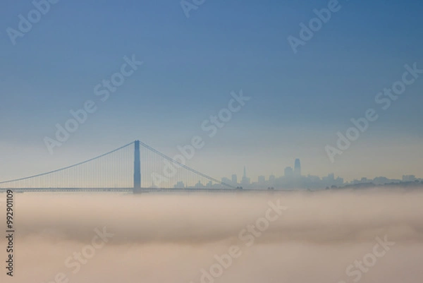 Fototapeta Golden Gate Bridge above fog with city skyline in distance on sunny day