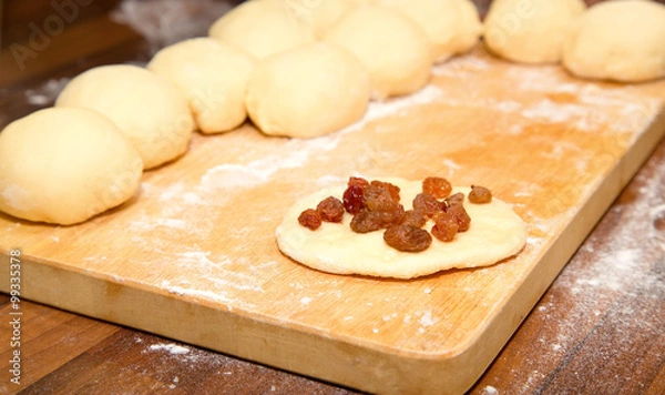 Fototapeta The cut dough for pies and one flat cake strewed with raisin on