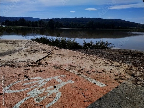 Fototapeta Bicycle path straight to water. Flood in Czech Republic. Road under water. Large amount of water on field. Disaster in Czech. Climate change. Clear blue sky after heavy rain. Weather in autumn.