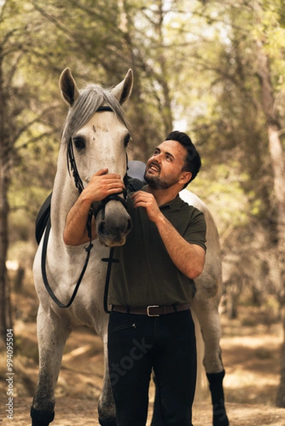 Obraz Man looks smiling at his horse during an equestrian route. Concept Love for animals. Vertical photo.