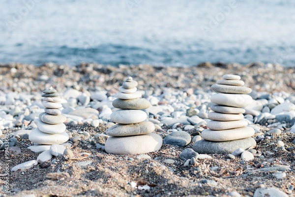 Fototapeta Stacking the equalizer stone on the blue beach with lots of pebbles around