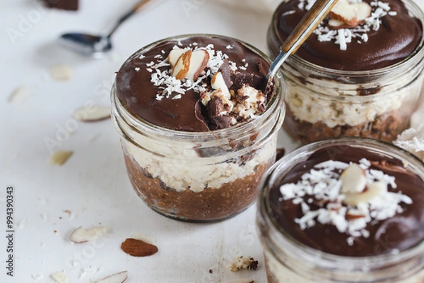 Fototapeta Three jars of homemade chocolate overnight oatmeal with shredded coconut and sliced almonds. Selective focus with blurred foreground and background. A joy to eat for breakfast or snack.