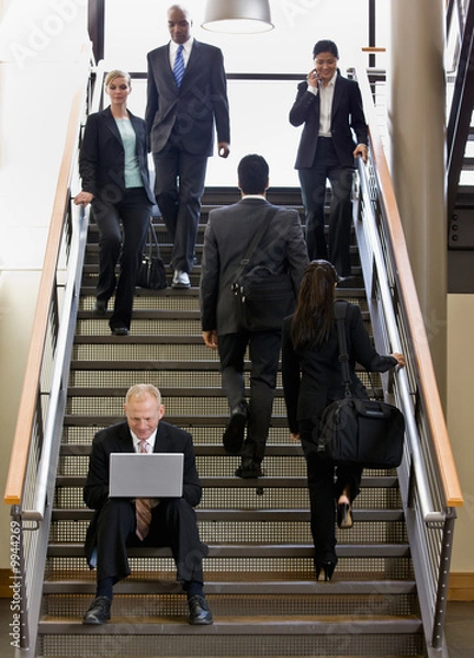 Obraz Businessman sitting and working on laptop on busy office stairs