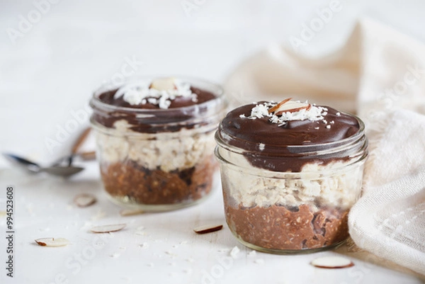 Fototapeta Two jars of homemade chocolate overnight oatmeal with shredded coconut and sliced almonds. Selective focus with blurred foreground and background. A joy to eat for breakfast or snack.