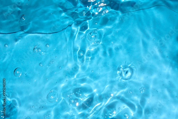 Fototapeta Blue water with ripples on the surface. Defocus blurred transparent blue colored clear calm water surface texture with splashes and bubbles. Water waves with shining pattern texture background.