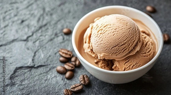 Fototapeta Two scoops of coffee ice cream in a white bowl with coffee beans scattered around it on a dark background.