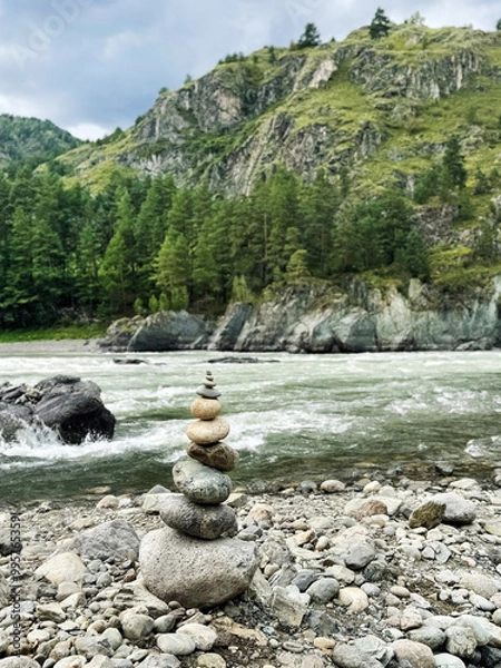 Obraz Round stones are balanced on top of each other, against the backdrop of a flowing river and rugged mountains, embodying the concept of natural balance. Altai, Russia