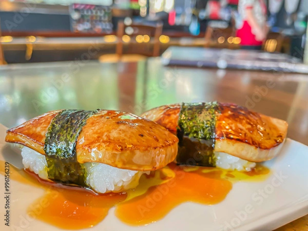 Obraz Close-up of two nigiri sushi, topping with foie gras. The elegant presentation is enhanced by the light reflections from the background, suggesting a vibrant sushi bar atmosphere.