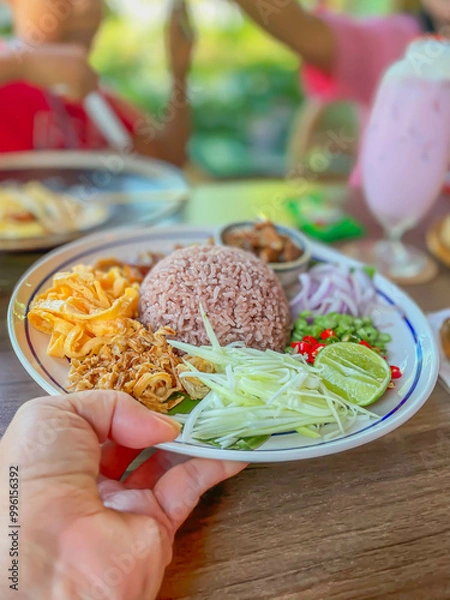 Obraz Closeup of shrimp paste fried rice thai food  held in a women hand with blurry background of people and dining atmosphere.