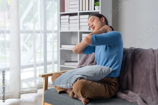 Fototapeta A woman is sitting on a couch with a pillow behind her back