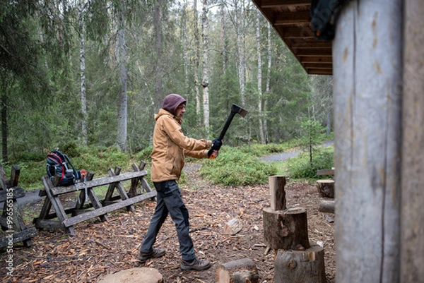 Fototapeta man chopping firewood with an axe for making a fire in the forest