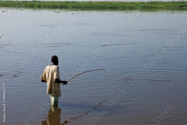 Fototapeta A man fishes along the shore of the White Nile River in South Sudan