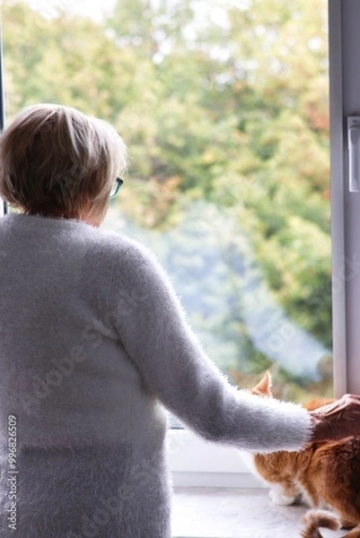 Obraz A lonely elderly woman standing at the window and waiting