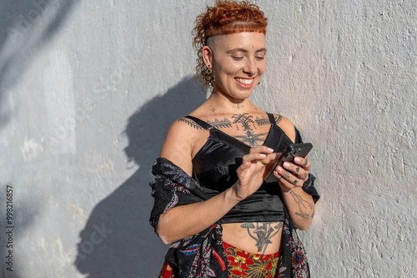 Obraz Cheerful woman using cellphone against wall on sunny day