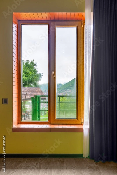 Fototapeta A spacious yellow room features a large wooden window, allowing natural light to illuminate the space while showcasing a vibrant green outdoor view