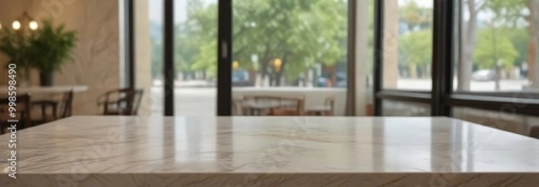 Fototapeta A marble countertop in a restaurant or cafe, with a blurred view of the outdoor seating area and trees through large windows