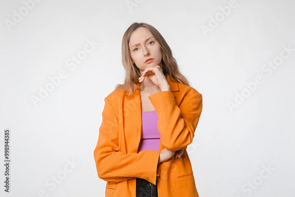 Fototapeta thoughtful and concerned young woman with a serious expression looking at the camera. Concept of introspection and concern. Female posing on a white studio background, wearing an orange blazer