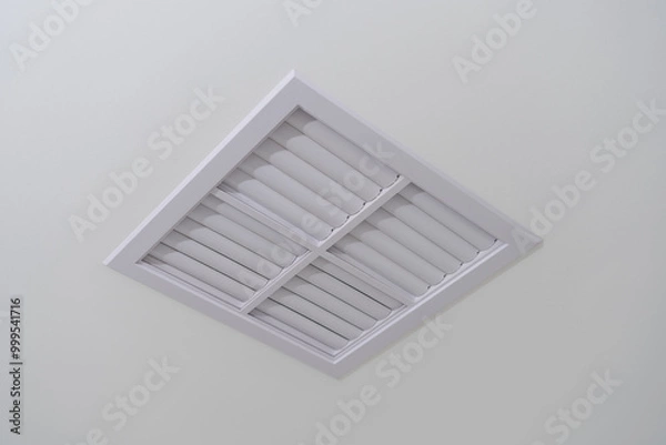 Obraz A white plastic ventilation grille with small holes for ventilation, installed on the ceiling to remove air from a room.