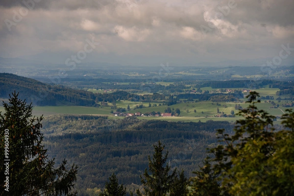 Fototapeta A panoramic view of Bavaria’s rolling hills, forests, and scattered farms under a cloudy sky, with distant villages nestled in the landscape..