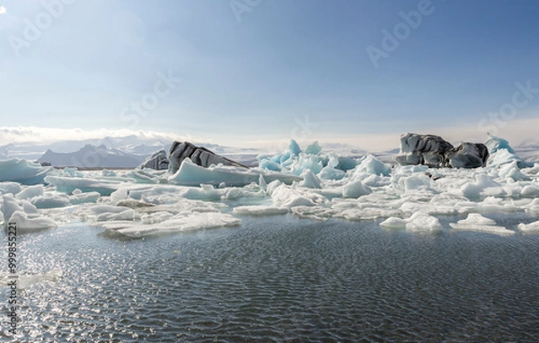 Fototapeta many blue, white and dark icebergs floating towards the Atlantic ocean, with snow-capped mountains in the background, Jökulsárlón Galcier Lagoon, Iceland