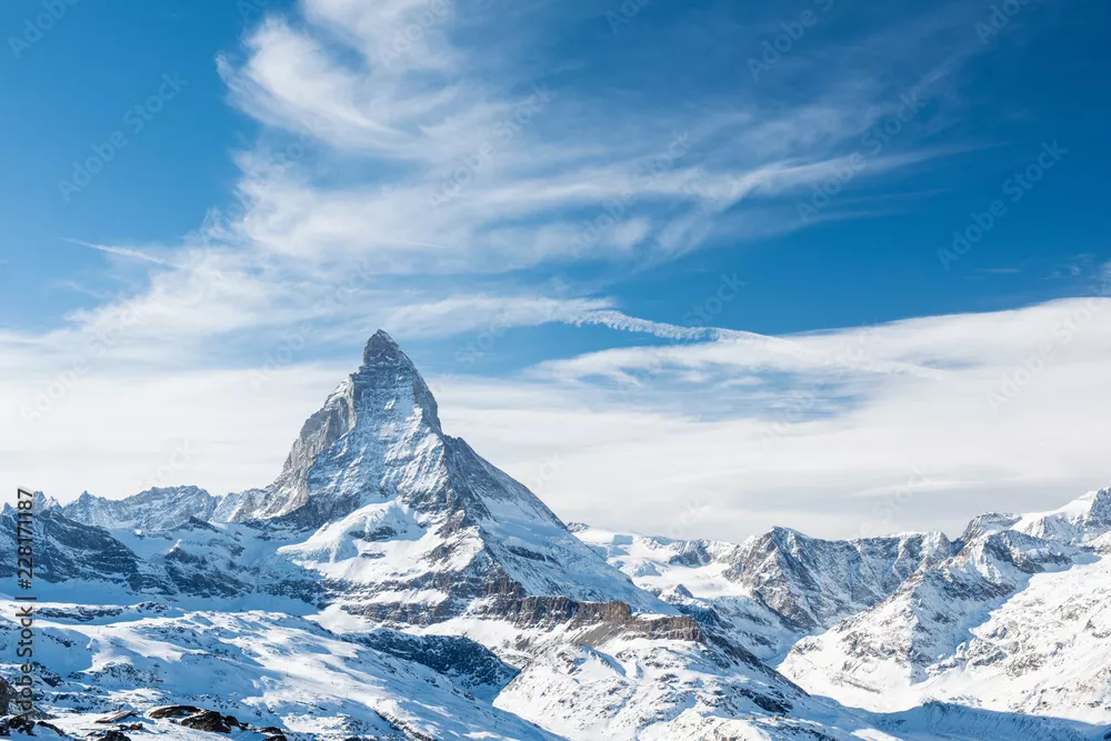 Fototapeta Malowniczy widok na ośnieżony szczyt Matterhorn w słoneczny dzień z błękitnym niebem i dramatycznymi chmurami w tle, Szwajcaria.
