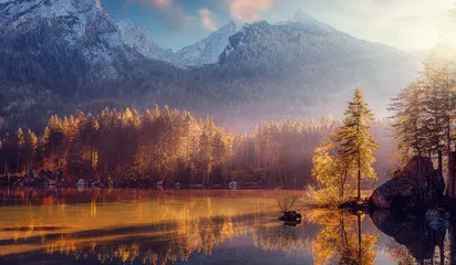 Fototapeta Niesamowita przyroda. Piękny krajobraz z wysokimi górami z oświetlonymi szczytami, kamieniami w górskim jeziorze, odbiciem, niebieskim niebem i żółtym światłem słonecznym o wschodzie słońca. Niesamowite tło natury.
