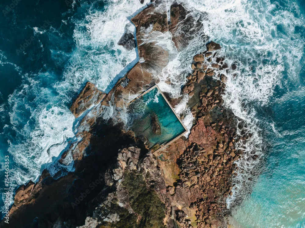 Fototapeta Widok z lotu ptaka światło wczesnego poranka z falami oceanu przepływającymi przez skały wokół oceanicznego basenu skalnego North Curl Curl podczas burzy.