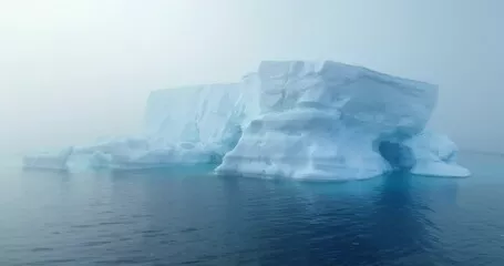Fototapeta Gigantyczna góra lodowa dryfuje poranną mgłą oceaniczną na Antarktydzie. Tajemnicza dramatyczna scena mgły. Topnienie lodowców, wpływ zmian klimatycznych na środowisko polarne. Podróże i eksploracja Antarktyki. Strzał z drona z bliska